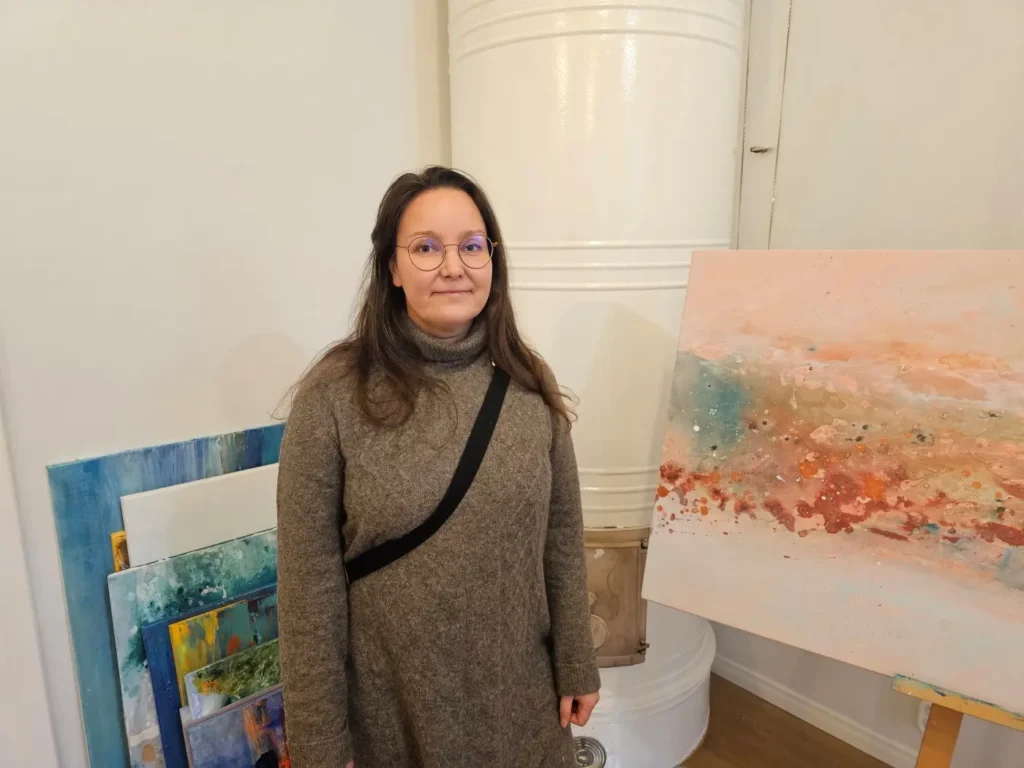 Kuvataitelija ja Magia Naturali yrityksen omistaja Katri Tupini poseeraa taideteostensa ympäröimänä.